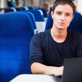Handsome young man using his laptop computer while on the train (shallow DOF; color toned image)