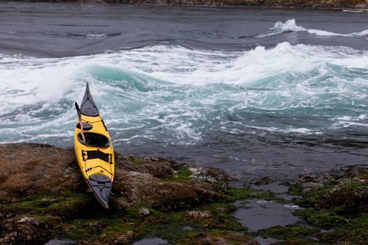 Colourful yellow sea kayak and paddle beached on a rocky ledge alongside whitewater tidal rapids