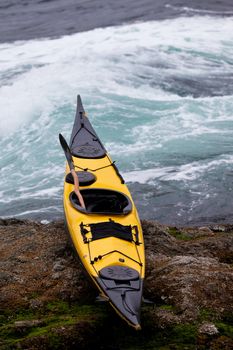 Colourful yellow sea kayak and paddle beached on a rocky ledge alongside whitewater tidal rapids