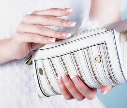 Beautiful female hands with manicure hold an open white handbag