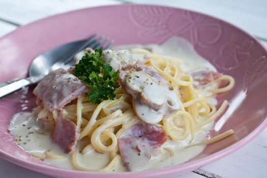 Spaghetti cream with bacon and parsley on pink dish.