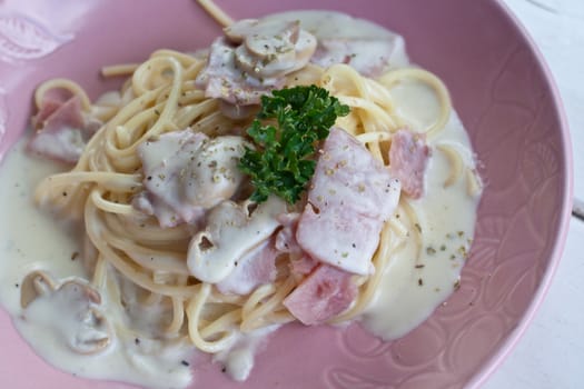 Spaghetti cream with bacon and parsley on pink dish.