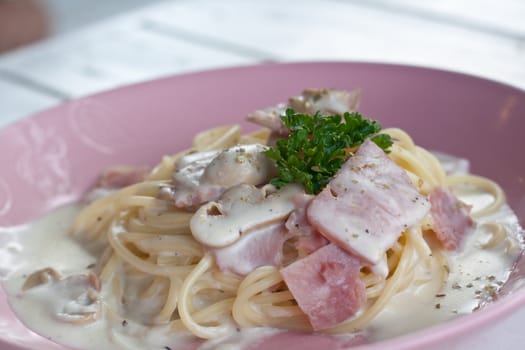 Spaghetti cream with bacon and parsley on pink dish.