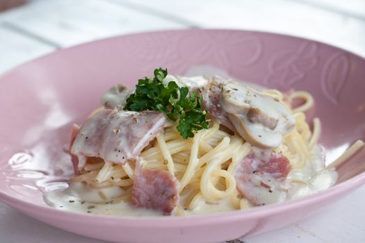 Spaghetti cream with bacon and parsley on pink dish.