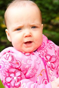 A young infant girl in pink is photographed outdoors for this child portrait.