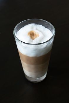 Glass with classic latte coffee layered with milk foam on dark wooden table