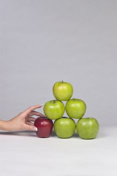 Woman's hand selecting the only red apple from a stack of mostly green apples