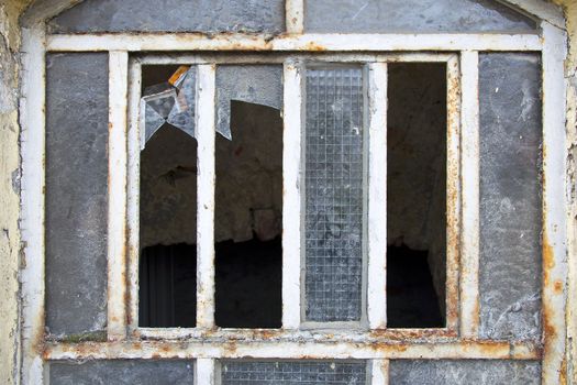 Broken vandalized window with rusty metal frame.