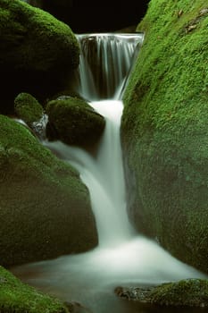 A small mountain stream waterfall through bright green moss covered rocks