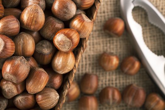 Whole hazelnuts in basket with nutcracker on table, from directly above.