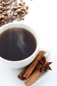 Cup of Hot Coffee with Cinnamon Sticks, Star Anise and Coffee Beans on a white table