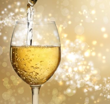 White wine being poured into a wine glass on shiny gold background