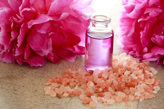 Aroma oil in bottle with pink peony flowers and bath salt