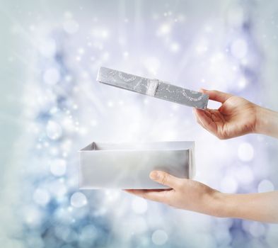 Woman opening a silver gift box on a blue holiday lights background 