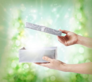 Woman opening a silver gift box on a green holiday lights background 