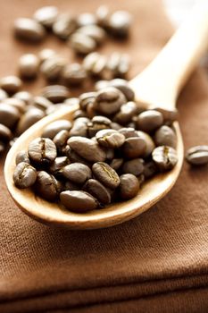 Coffee beans in wooden spoon on brown cloth