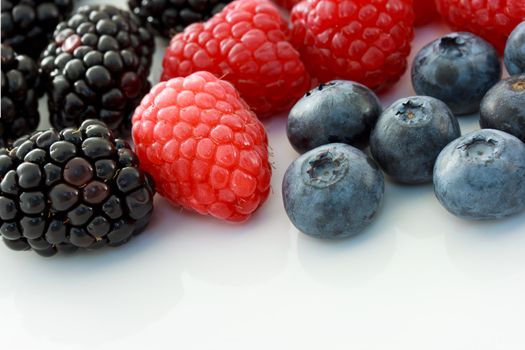 Raspberries, blueberries and blackberries on white ceramic plate