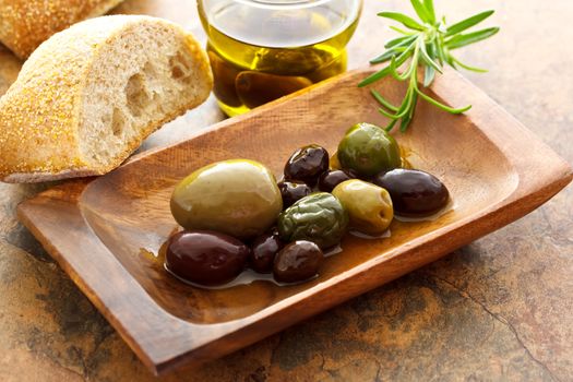 Olives on wooden plate with bread and rosemary