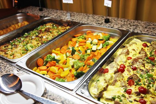 Delicious hot buffet at a catered event with large stainless steel dishes filled with an assortment of fresh vegetables