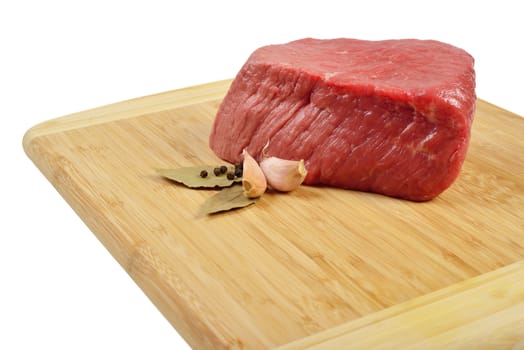 Piece of raw beef on a wooden board, decorated with garlic and bay leaves.