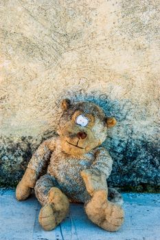 A dirty and old teddy bear against a grunge wall