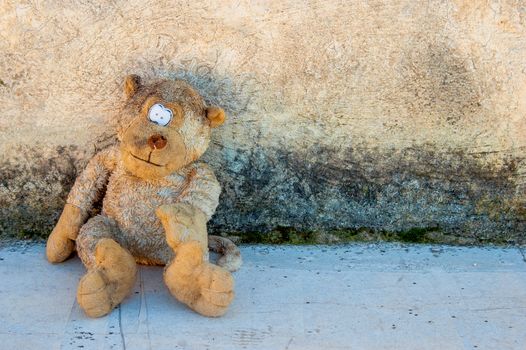 A dirty and old teddy bear against a grunge wall