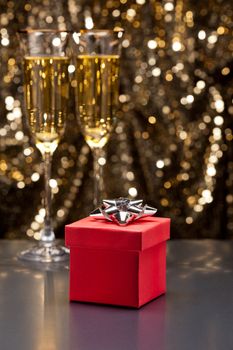 Champagne glasses and gift in front of gold glitter background