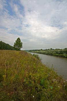 View of river, forest and field in summer against  blue sky, Russia.