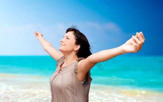 Beautiful young woman with arms raised standing on beach