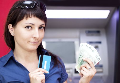 Beautiful woman using credit card, she is withdrawing money from an ATM machine.