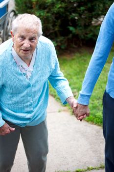 Senior lady walking with caregiver, holding hands