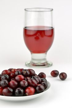 Close-up of fresh cranberries with a glass of healthy juice on white background. Focus on cranberries.