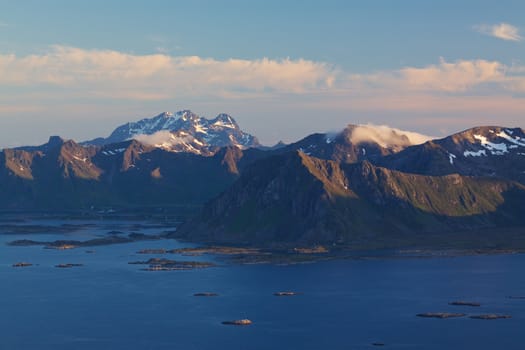 Picturesque mountain range on Lofoten islands in Norway lit by midnight sun with tiny rocky islands in the sea