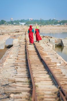 Female indian workers go along railway and lake, rear view