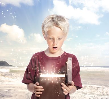 Happy Young Blonde Boy Opening a Gift Box on the Beach