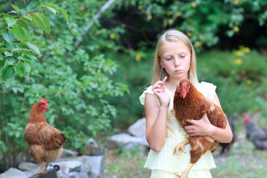 Young Blonde Girl in the Garden with Chickens in a Yellow Dress