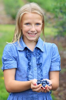 Young Blonde Girl Holding Fresh Picked Blueberries in a Blue Dress Smiling