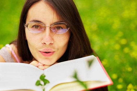 Closeup portrait of a young  female with a book  on a green meadow