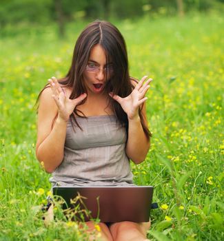 Shocked Young woman using her laptop outdoors.