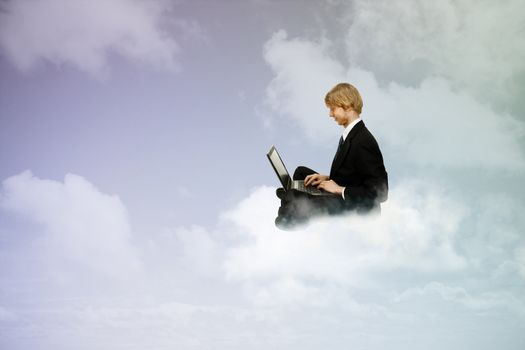 Young business man sitting atop the clouds using a laptop 