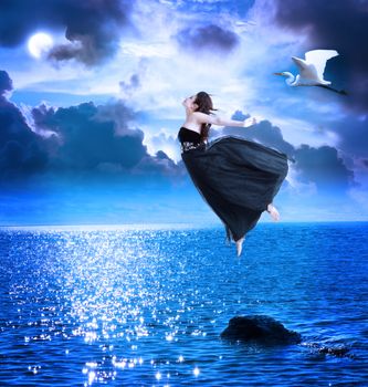Beautiful girl jumping into the blue night sky with white egret