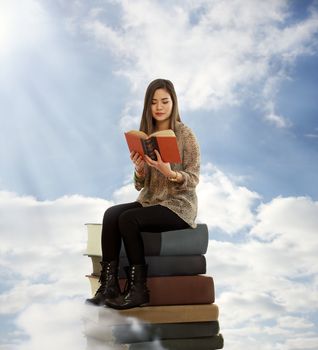 Beautiful Young Woman Reading a Book on Top of Books in the Clouds