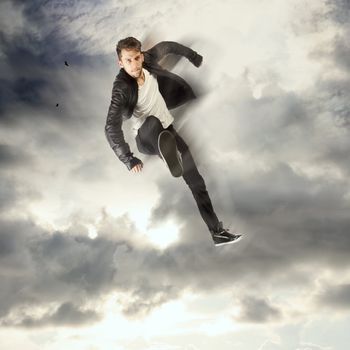Cool young man jumping and kicking in the cloudy sky