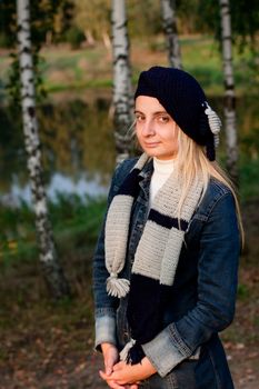 A blonde girl in a beret and scarf and jeans coat in a forest
