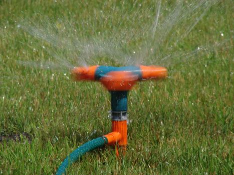 Moving streams of sprayer watering green grass lawn