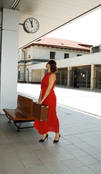 woman with a suitcase looks at the clock while standing on the platform