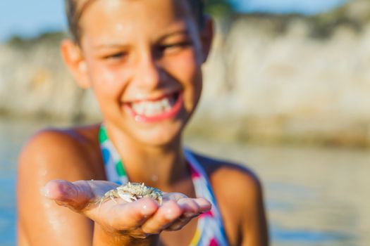 Adorable happy girl holding crab on hand on the beach. Focus on the crab.