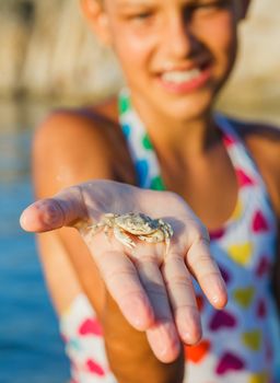Adorable happy girl holding crab on hand on the beach. Focus on the crab. Vertical view