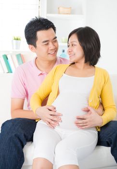 Asian Chinese couple. Husband and 8 months pregnant wife sitting on sofa