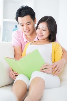 Asian couple reading book on sofa happily